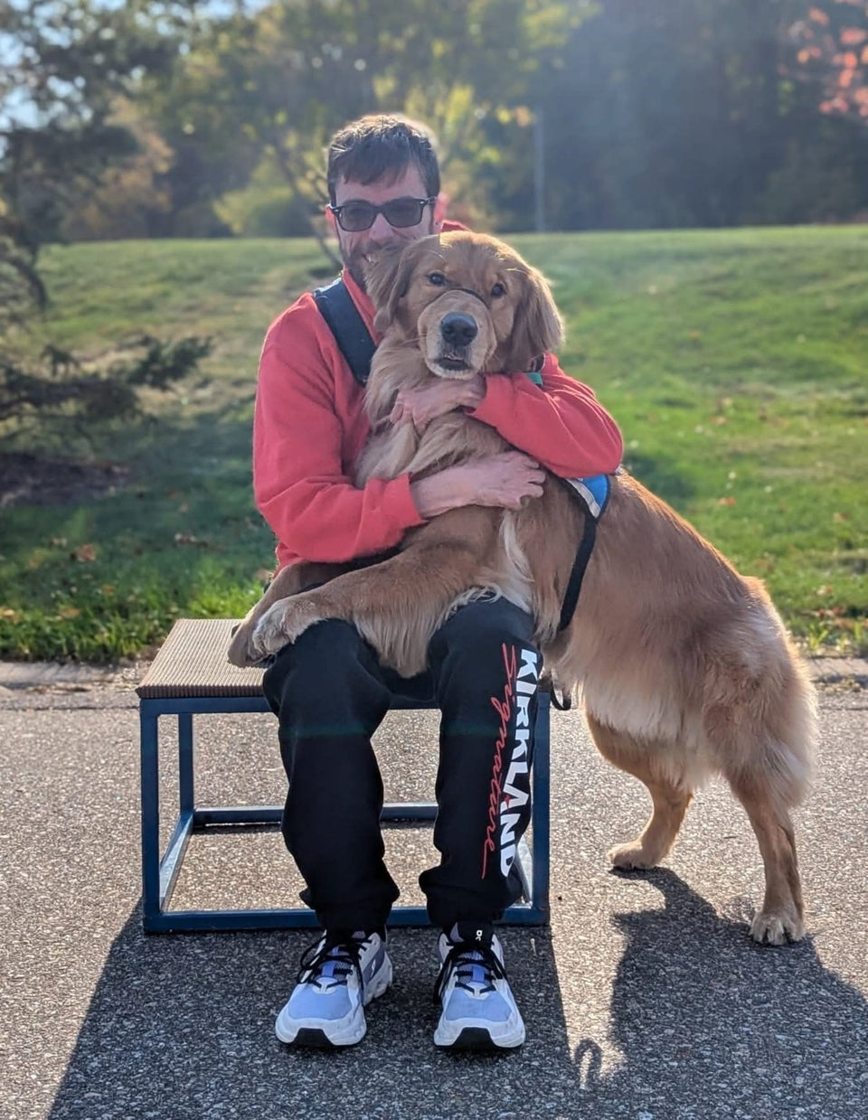 PuzzlePup founder Mike hugging his Helping Paws service dog Normie, a golden retriever in a service vest, outdoors