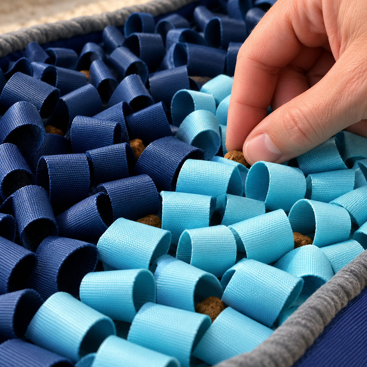 A hand tucking kibble deep between the SmartMat's navy and aqua fabric loops
